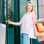 Moteris su pirkinių krepšiais eina pro parduotuvės duris